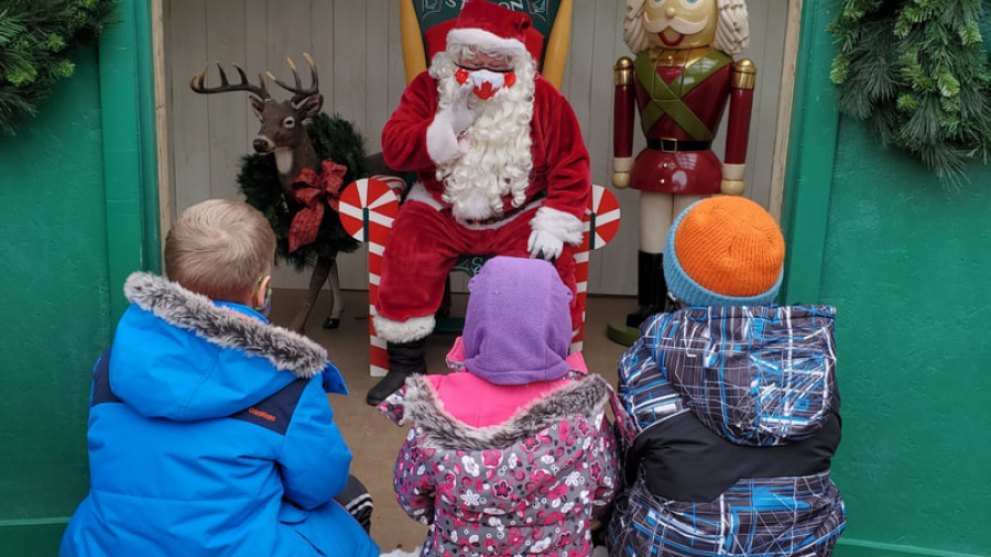 a picture of Santa speaking to three kids at apple land station 