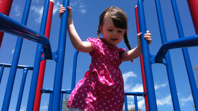 little girl playing on a playground  wearing a pink dress with white and two pig tail braids.