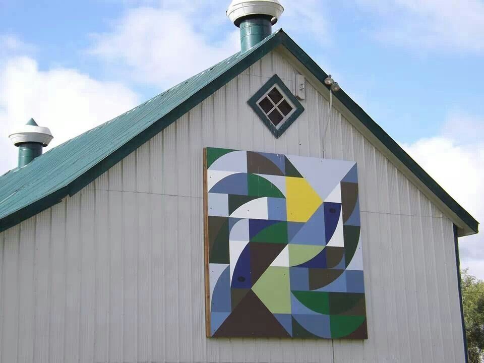 A green and white barn adorned with a kaleidoscope quilt-style mural.
